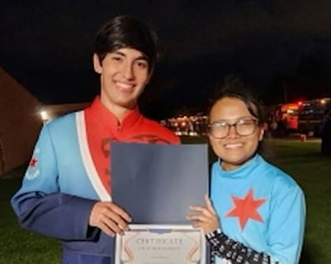 Two students in the Pride of Syracuse City School District Marching Band pose with an award. The musicians are dressed in the marching band’s new uniforms, which are inspired by the Syracuse city flag.